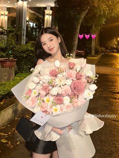 a woman holding a large bouquet of flowers in her hands while standing on the street