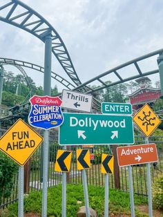 several street signs are posted in front of a roller coaster at an amusement park,