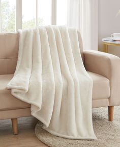 a couch with a white blanket on top of it next to a chair and window