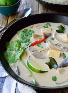 a black bowl filled with soup and garnished with cilantro, green peppers, limes, and tofu