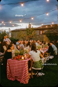 a group of people sitting around a table with food on it and lights strung above them