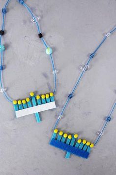 two necklaces made out of lego blocks on a gray surface, one with yellow and blue beads