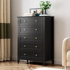 a black chest of drawers in a living room next to a chair and potted plant