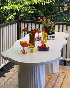 a white table with flowers and wine glasses on it, sitting in front of a balcony