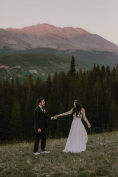 a bride and groom holding hands in the mountains