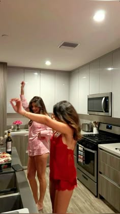 two women standing in a kitchen next to an oven and stove top with one pointing at the other