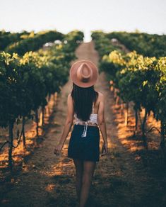 a woman wearing a hat walking through a vineyard