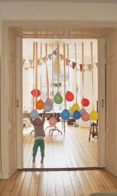 a young boy standing in front of an open door with balloons hanging from the ceiling