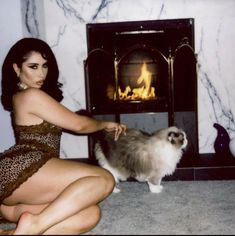 a woman kneeling down in front of a fire place with a cat on the floor