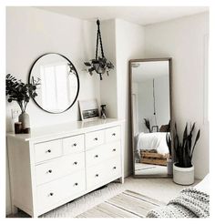 a bedroom with white furniture and plants on the dresser next to a large round mirror