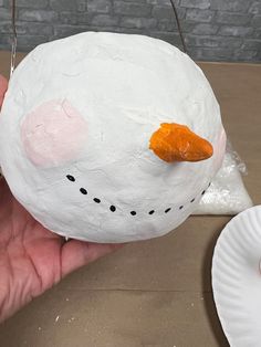 a hand holding a paper plate with a snowman face on it, and another person's hand holding a white paper plate with an orange carrot sticking out of its nose