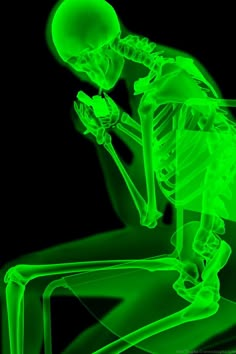 a green skeleton sitting on a chair with his hands in his knees and looking down