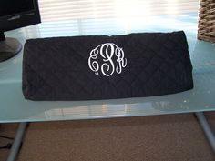 a black monogrammed pillow sitting on top of a glass table next to a computer