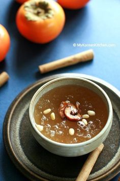 a bowl of soup on a plate next to some oranges and cinnamonsticks