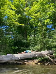 a woman laying on top of a fallen tree over water