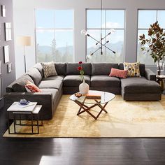 a living room filled with lots of furniture in front of two large windows and a rug on the floor