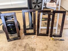 three wooden frames sitting on top of a floor next to a white car in a garage