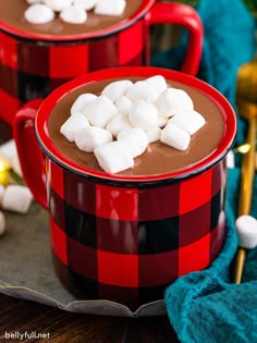 two red mugs filled with hot chocolate and marshmallows on a table