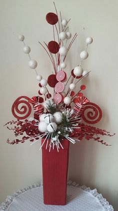 a red vase with white balls and candy canes in it sitting on a table