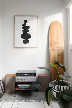 a record player sitting on top of a wooden shelf next to a plant and a surfboard