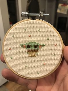 a hand holding a cross stitch star wars baby yoda