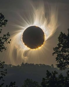 the sun is partially obscured by clouds as it transits across the sky in front of trees