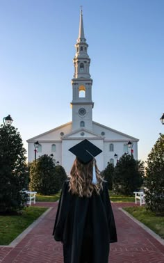 a woman wearing a graduation cap and gown standing in front of a white building with a steeple