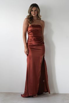 a woman in a long red dress standing next to a white wall and posing for the camera