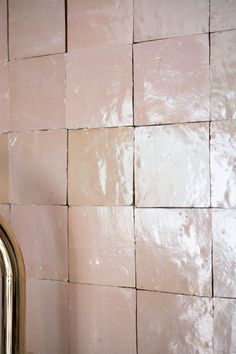 a bathroom wall with pink tiles and a shiny metal faucet next to it