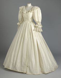 a white dress with ruffles on the sleeves and neckline is displayed in front of a mannequin