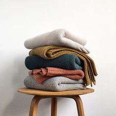 a stack of folded sweaters sitting on top of a wooden stool