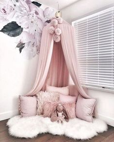 a pink canopy bed with white fluffy pillows and flowers on the wall behind it in a girls'bedroom