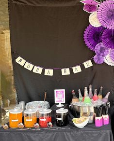 a table topped with lots of drinks and desserts next to a purple flower wall