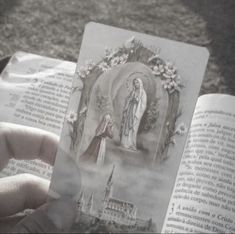 a person holding an open book in their hand with the image of mary and jesus on it