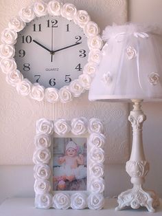 a white clock sitting on top of a table next to a lamp and photo frame