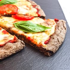 two slices of pizza with tomatoes and basil on top, sitting on a slate board