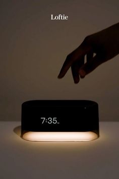 a person touching the time on an alarm clock that is lit up in front of them