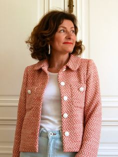 a woman standing in front of a white door wearing a red jacket and blue jeans