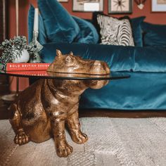 a bronze hippo sitting on the floor with a glass table in front of it