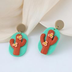 a pair of earrings with flowers on them sitting in front of a white fabric curtain