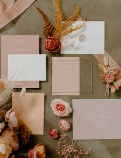 the wedding stationery is laid out with flowers and feathers