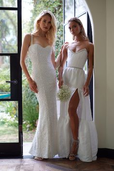 two beautiful women standing next to each other in front of an open door wearing white dresses