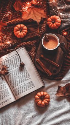 an open book and cup of coffee on a bed next to pumpkins, leaves and candles