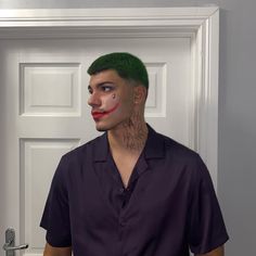 a man with green hair wearing a clown nose paint on his face and shirt is standing in front of a door