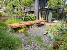 a wooden bench sitting in the middle of a garden next to tall grass and trees