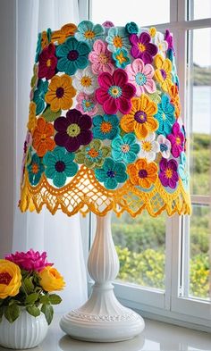 a crocheted lamp shade sitting on top of a table next to a vase with flowers