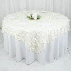 a round table with white linens and flowers on it is set up for a formal function