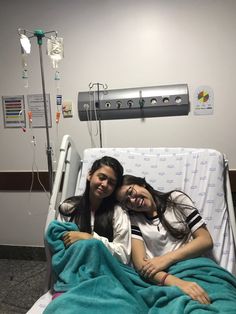 two young women laying in a hospital bed with their arms around each other and smiling at the camera