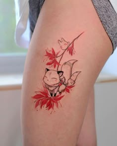 a woman's thigh with red leaves and a cat tattoo on the side of her leg