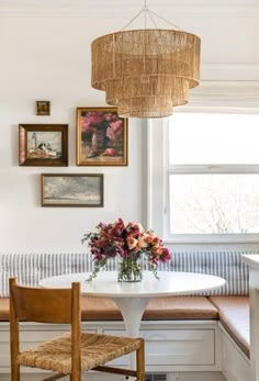 a dining room table with flowers on it and pictures hanging above the table, along with two chairs